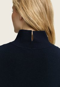 Donkerblauwe gebreide trui met een hoge geribde kraag en een split aan de achterkant, met een gestructureerde stof en een aansluitend ontwerp.