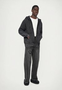 Mörkgrå luvtröja med texturerad yta, kombinerad med ledigt sittande mörkgrå jeans som har sidofickor och en subtil design.