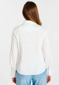 Wit overhemd met lange mouwen en een kraag, voorzien van een getailleerde pasvorm en knoopmanchetten. Gladde textuur met een subtiele glans.