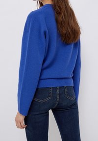 Pull en maille bleu avec un col rond, un ourlet côtelé et une coupe ample. Associé à un jean en denim foncé, mettant en valeur une tenue décontractée.