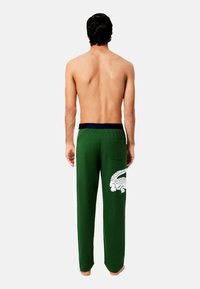 Zöld melegítőnadrág kék derékrésszel, fehér oldalsó panellel és egy nagy fehér krokodil mintával a hátsó zseben.