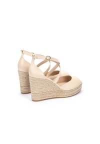 Sandales compensées en cuir beige avec des sangles entrecroisées, plate-forme en jute tissé et un design à bout rond. Bride de cheville ajustable avec une boucle.
