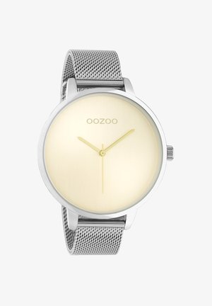 Montre ronde en métal avec un bracelet en maille argentée, cadran doré clair, design minimaliste, aiguille des heures et des minutes dorées. Logo de la marque : OOZOO.