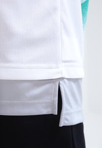 Vit kortärmad skjorta med ett strukturerat, andningsbart tyg. Sidslitsar vid fållen. Inga synliga mönster. Enkelt design, rena linjer.