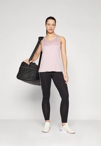 Světle růžový tílko bez rukávů, černé legíny s bočními pruhy, bílé tenisky s fialovými detaily a černá sportovn�í taška.