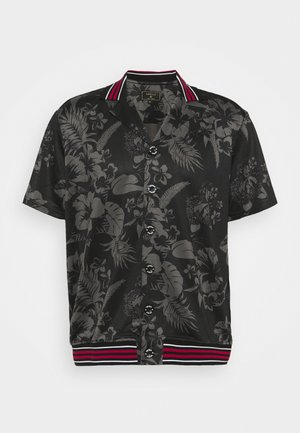 Lyhythihainen musta paita, jossa on tumma kukkakuosi. Paidassa on laskostettava kaulus, mustat napit ja raidallinen punavalkoinen helma.