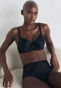 Black bra with molded cups and adjustable straps, paired with high-waisted black briefs featuring mesh accents and a smooth texture.