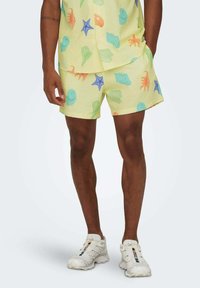 Camisa corta de manga corta amarilla con estampado y pantalones cortos a juego con diseños de conchas y estrellas de mar; tejido texturizado, corte relajado, combinada con zapatillas blancas.
