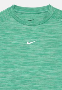 Zöld sportpóló, texturált anyagból, kerek nyakkivágással és fehér Nike logóval a mellkasán.