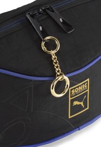 Borsa in tessuto nero con cerniera blu, dettagli in catena dorata e un logo dorato con Sonic the Hedgehog e il marchio Puma.