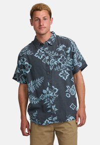 Camisa de manga corta, con botones, en tela oscura con un gran patrón floral en azul claro y sutiles diseños de hojas; presenta un bolsillo en el pecho.