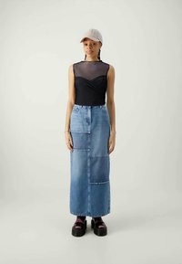 Svart mesh tank topp med vridd design, kombinert med en lys blå denim maxi skjørt med lappeteppe-seksjoner. Svarte platå sko.