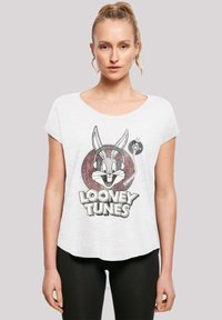 Bílý tričko s krátkým rukávem s grafikou Bugs Bunnyho se sluchátky, text "Looney Tunes" pod ním a kulatým akcentem na boku.