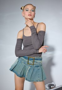 Siva majica dugih rukava i plava denimska plisirana suknja sa širokim pojasom. Suknja ima izblijedjeli uzorak i zlatni akcent kopče.