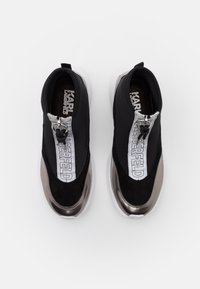 Czarne i srebrne sneakersy wsuwane z białymi podeszwami, sygnowane marką "Karl Lagerfeld", z zamkiem błyskawicznym z przodu i pętlą do zakupu na białym tle.