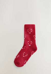 Piros bolyhos zokni puha tapintással, fehér karácsonyi cukorpálca mintákkal díszítve, és egyszínű piros szegéllyel.