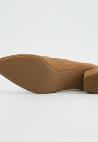 Chaussure à talon haut en daim marron clair, avec un bout pointu, une tige texturée, et une semelle en caoutchouc ornée d'un logo subtil sur le côté.