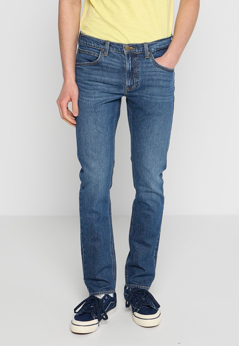 Niebieskie dżinsy o prostym kroju, z pięcioma kieszeniami i subtelnym wyblaknięciem. W połączeniu z granatowymi trampkami i jasnobiałą koszulką.