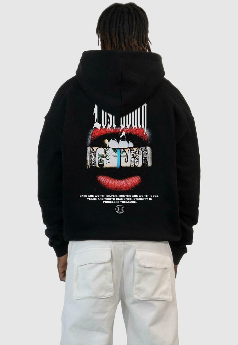 Black hoodie featuring a graphic design of red lips and money, with white text stating motivational phrases, worn over white pants.