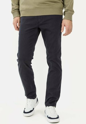 Donkerblauwe denim jeans met een slim fit en zichtbare stiksels, gecombineerd met witte sneakers met marineblauwe accenten en gestructureerde zolen.