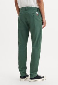 Pantalons en coton verts à coupe droite, avec deux poches arrière et une petite étiquette de marque. Présente une texture lisse et une taille standard.