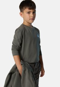 Camiseta de manga larga gris hecha de algodón, con un cuello redondo y un pequeño logo circular azul. Combinada con pantalones grises a juego.