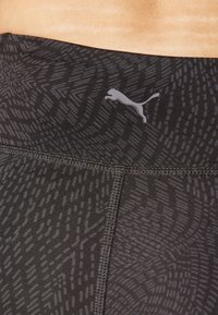 Leggings noirs à motif présent avec un subtil design géométrique, affichant une texture lisse et un petit logo gris sur la taille.