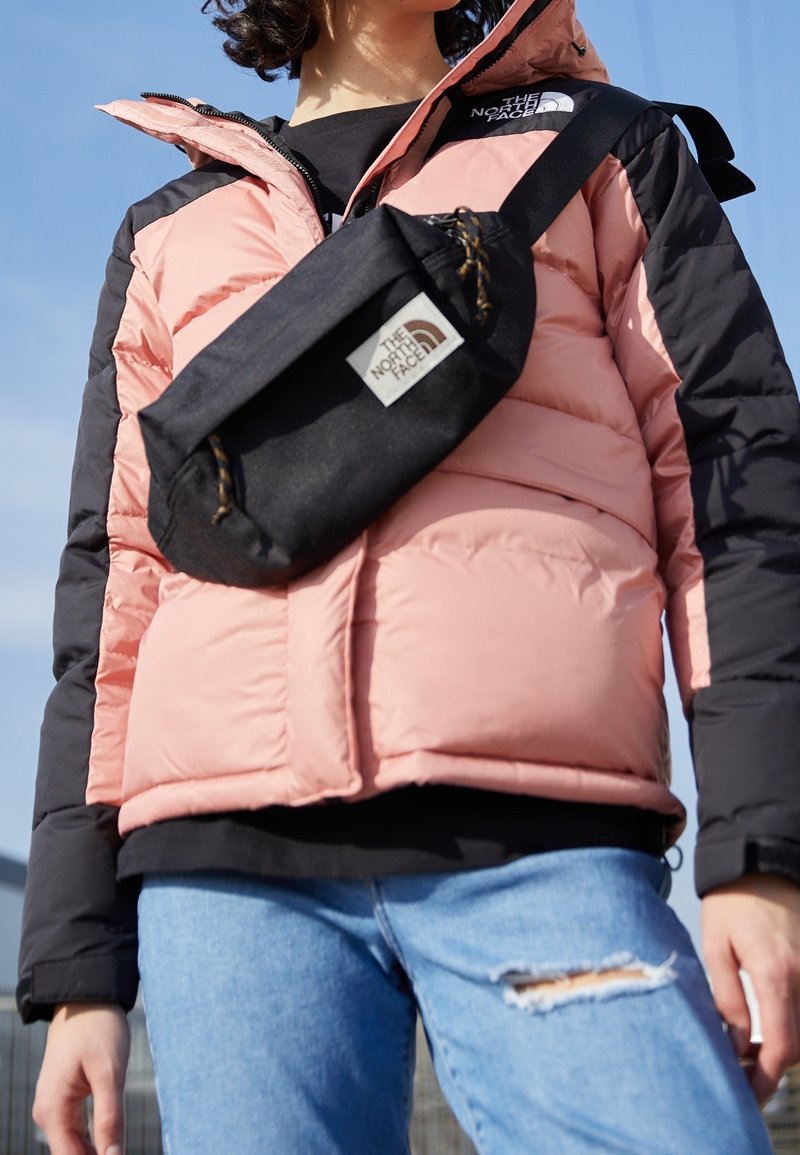 Puffy pink and black jacket with a high collar, accompanied by a small black crossbody bag featuring a logo. Blue distressed jeans.
