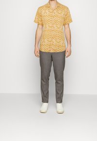 Camisa amarilla de manga corta con un patrón geométrico, combinada con pantalones grises y zapatillas blancas. Tela suave y corte relajado.