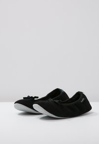 Black ballet flats made of soft fabric with a smooth gray sole, featuring a small bow accent on the front and a textured interior.