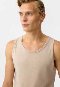 Licht beige tanktop van zachte katoen met brede schouderbanden en een ronde halslijn. Vlotte textuur en minimale naden.