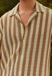 Koszula z krótkim rękawem z wzorzystym wzorem naprzemiennych brązowych i kremowych pasków. Materiał wydaje się lekki o teksturowanym wykończeniu.