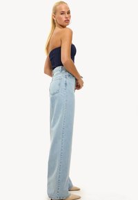 Lichtblauwe high-waist jeans met een rechte pijp, gemaakt van denim. Het model draagt een marineblauwe strapless top en beige spitse hakken.