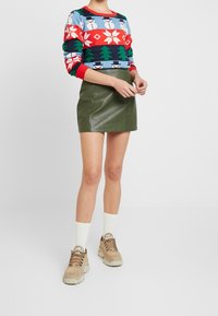 Färgglad stickad tröja med snögubbar och träd, kombinerad med en grön skinnimitation kjol. Beige klumpiga sneakers och vita strumpor fulländar outfiten.