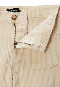 Pantalon en velours côtelé couleur crème avec fermeture éclair, bouton et une poche avant. Présente une texture côtelée verticale et un matériau doux.