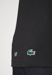 Camisa negra de textura suave, con un logo de cocodrilo en verde y blanco y el texto "ULTRA DRY" en la parte inferior izquierda.