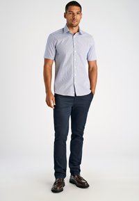 Camicia a maniche corte con bottoni di colore azzurro chiaro con un motivo a righe sottili, abbinata a pantaloni slim-fit blu scuro e scarpe in pelle marrone.