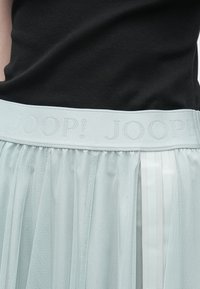 Φούστα από ανοιχτό γαλάζιο διαφανές τούλι με υφασμένο ζωνάρι στη μέση που φέρει το λογότυπο "JOOP!". Διαθέτει κάθετες σατέν ρίγες στο πλάι.