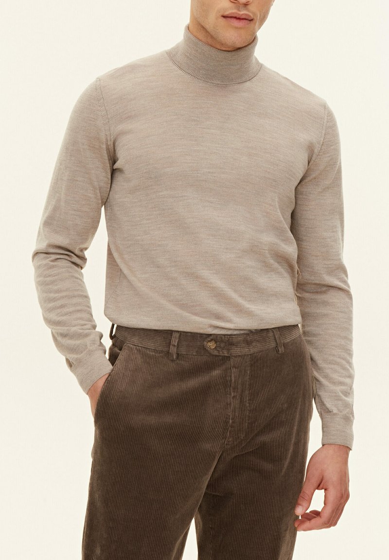 Hellbeige Rollkragenpullover mit langen Ärmeln und geripptem Hals. Kombiniert mit strukturierter, brauner Cordhose, die subtile Streifen zeigt.