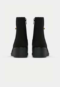 Botas de tornozelo pretas com acabamento em camurça, apresentando bico arredondado, salto bloco médio e detalhes em dourado nos zíperes traseiros.