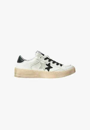 Witte lage sneaker met zwarte hieltab, zwarte en beige sterrenapplicaties aan de zijkant, zwarte veters en een beige rubberen zool met versleten details.