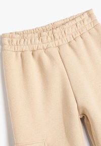 Beige sweatpants med elastisk talje og synlige syninger, lagt fladt på en hvid baggrund.