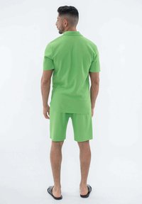 Polo court à manches courtes vert et shorts assortis en tissu léger. Design simple sans motifs, associé à des tongs noires.