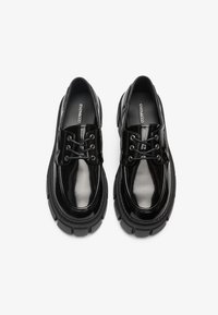 Črne lakirane čevlje s okroglim prstom, vezalnim dizajnom in debelim črnim gumijastim podplatom. Imajo okrasne šive in gladko sijajno površino.