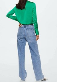 Grüne Langarmbluse mit glatter Textur, kombiniert mit hoch taillierten, hellblauen, weiten Jeans mit Gesäßtaschen.