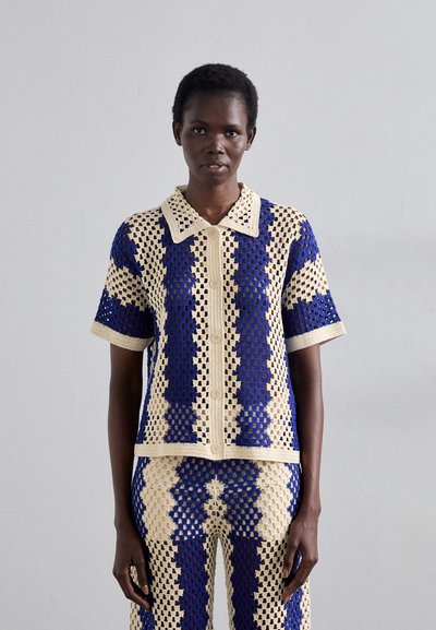 Ensemble au crochet dans des tons crème, bleu et marine ; chemise à manches courtes avec col et fermeture à bouton ; pantalon assorti avec un design à motifs similaire.