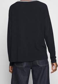 Svart långärmad topp med randig krage, avslappnad passform och mjuk textur. Kombinerad med mörka denimbyxor och kontrasterande sömmar.