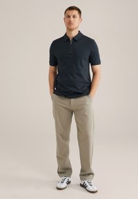 Polo de color marino con cuello con cremallera y bolsillo, combinado con pantalones caqui claros y zapatillas blancas con rayas negras. Diseño simple y moderno.