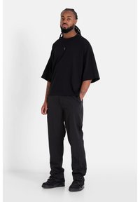 Svart oversize t-shirt med rund halsringning och korta ärmar, ihop med svarta tapered byxor och svarta sneakers. Slät textur genom hela plaggkombinationen.