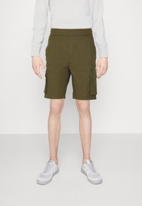 Shorts cargo verts olive avec une taille élastique, des poches latérales et une coupe décontractée, accompagnés de baskets grises claires.
